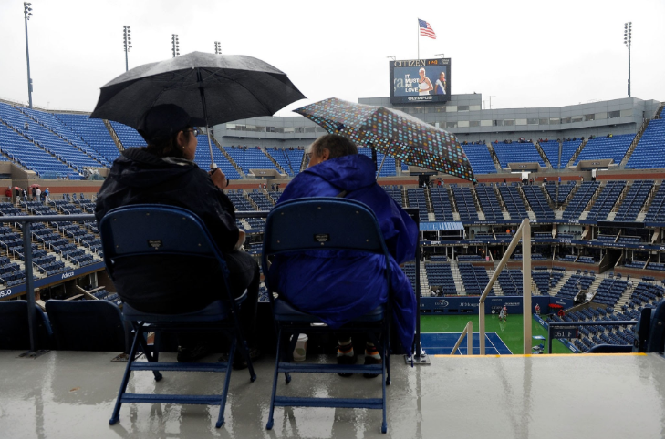 Fans under umbrellas during US Open rain delays.
